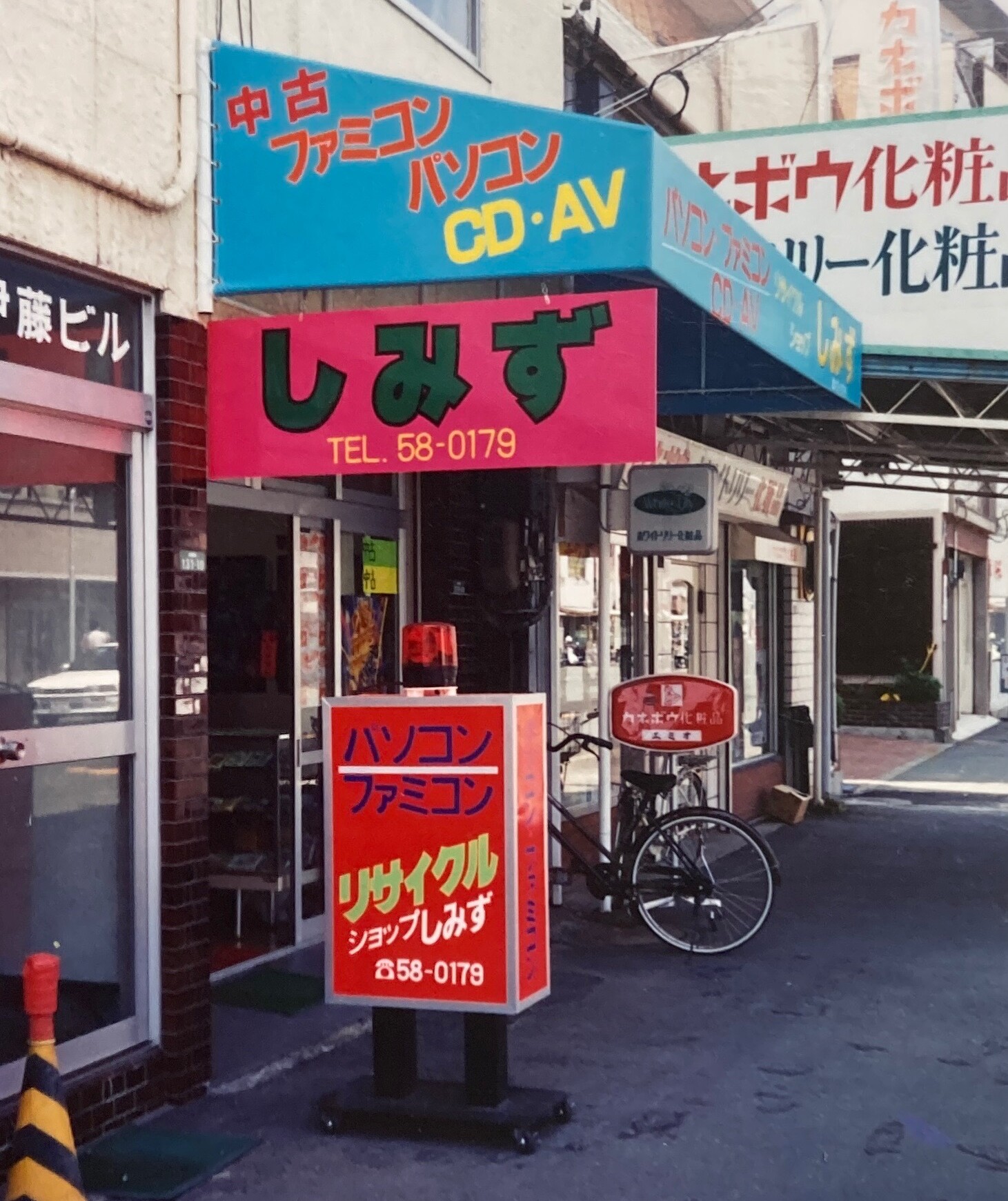 The storefront of 'Shimizu' — my father's shop in Toyohashi, circa 1986-1990. The sign reads 中古ファミコン パソコン CD・AV (Used Famicom, PC, CD & AV) and TEL 58-0179.